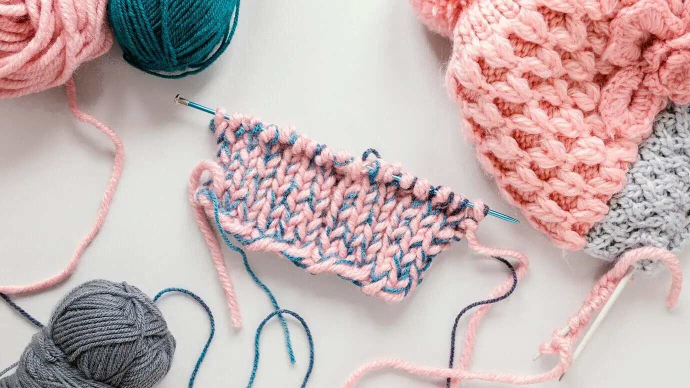 Draufsicht auf Stricknadeln und Wolle für eine Mütze.